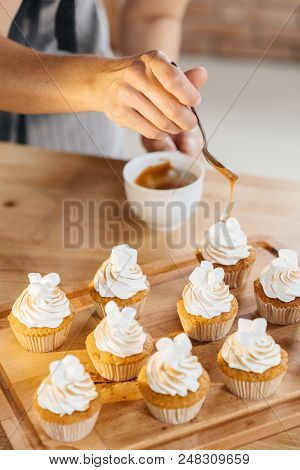 Woman Confectioner Pours Caramel From A Spoon On Juicy Capcake Muffins. Making Sweets.