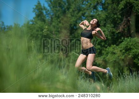 Young Woman Jumping On Background Of Trees. The Girl Is Engaged In Sports.