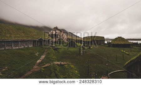 Old Viking Village In Iceland With Foggy Hill. Old Wooden Buildings Covered Grass