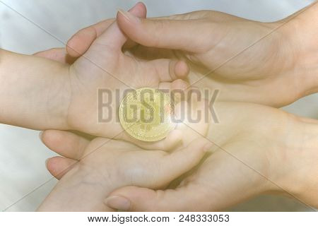 Bitcoin Concept. Children Share Bitcoin. Child Hand And Bitcoin. Bitcoin Shines With Bright Rays.