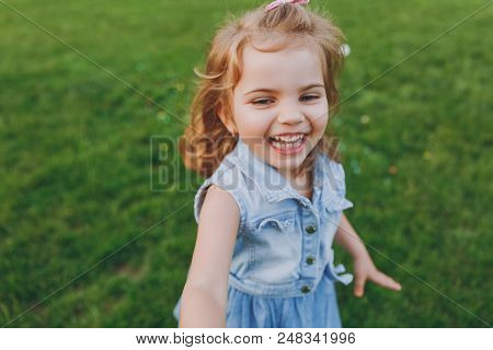 Joyful Little Cute Child Baby Girl In Denim Dress Walking And Running, Have Fun On Green Grass Lawn 