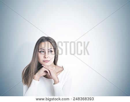Head And Shoulders Portrait Of A Beautiful Young Woman With Fair Hair Wearing White And Thinking Loo