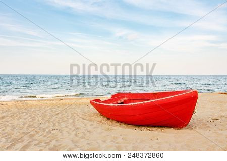 Old Red Fishing Boat On The Sandy Beach, Waves On The Water And Clouds Background