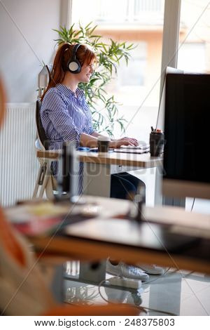 Woman with head phones working in modern office at computer