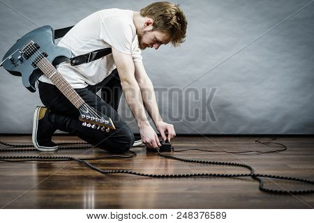 Man With Musical Instrument Setting Up Guitar Audio Stomp Box Effects And Cables In Music Studio