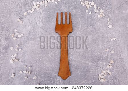 A Wooden Fork Is Situated On The Grey Tabletop, Surrounded With White Decorations.