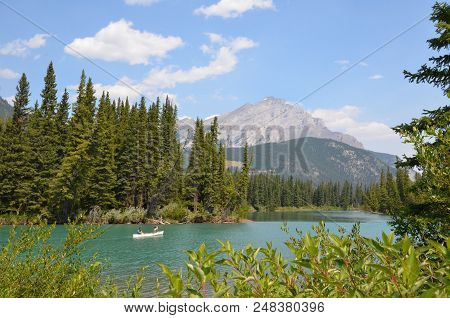 Banff, Ab / Canada - July 27, 2017:  Canoers Travel Down The River Near The Walkway Behind Cave And 