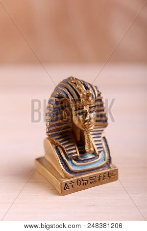 An Original Figure Of A Golden Sphinx With Striped Cap Is Situated On The Wooden Background.