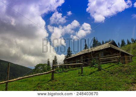 Photo Of Kolyba In Mountain Village In The Summer Under Beautiful Cloudy Sky. Ukraine, Carpathians, 
