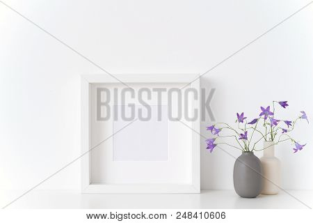 White Square Portrait Frame Mockup With Spring Bellflowers In Vases Near White Wall On White Backgro