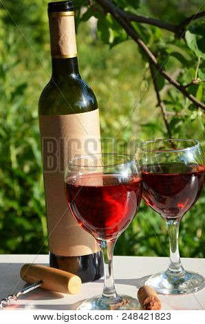 Red Wine Poured Into Wine Glass On Background Of Green Tree Leaf Foliage. Purpie Flower