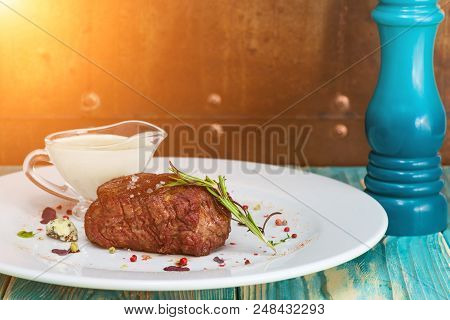 Close-up Appetizing Beef Steak With Herbs And White Sauce On A White Plate, On Awooden Table. Ray Of