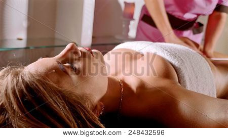 Massage Concept. Beautiful Young Woman Reciving Relaxing Massage At Luxury Spa Salon With Warm Cozy 