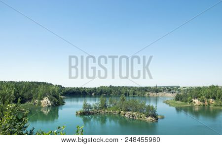 An Island In The Shape Of An Arc In The Middle Of A Large Lake Near The Rocks, Blue Clear Sky An Isl