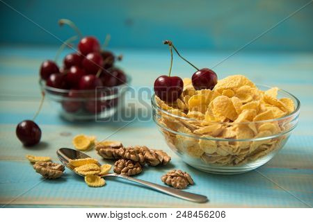 Tasty Cornflakes Witt Walnut And Cherry In Glass Bowl On Blue Background. Corn Flakes