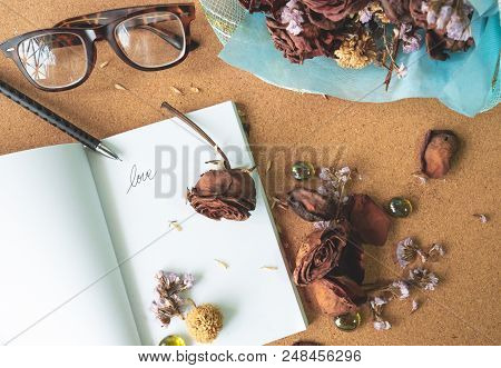 Top View Flat Layer Withered Old Rusty Brown Roses And Love Word  On Blank White Book With Blurry Gl