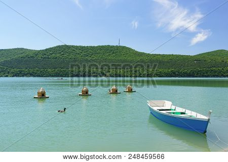 Bright Blue Empty Rowing Boat And Duck Houses On The Green Water Of The Mountain Lake Abrau-durso