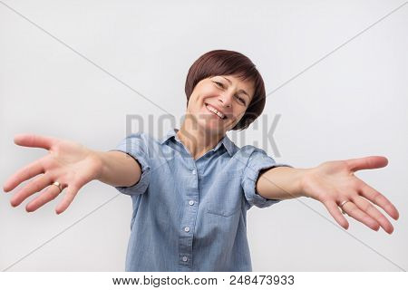 Portrait Of Attractive Mature Woman Raised Up Arms Hands At You. She Is Dressed In Blue Shirt. Happy