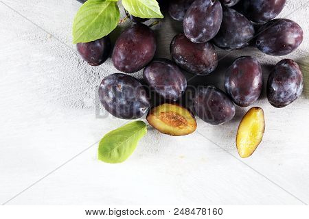 Plums On White Stone Background. Half Of Blue Plum Fruit. Many Beautiful Plums With Leaves.