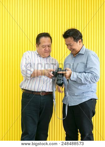 Photographer And Client Medel Checking Photo From Digital Camera Against Yellow Wall Background.