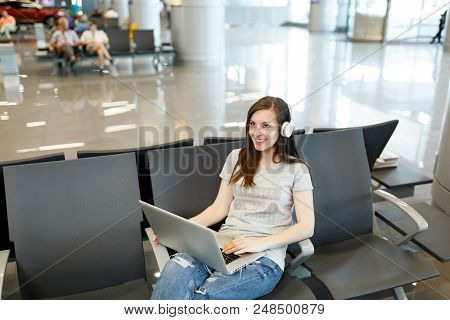 Young Smiling Traveler Tourist Woman With Headphones Listening Music Working On Laptop, Wait In Lobb
