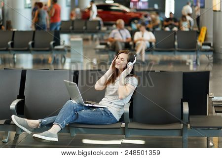 Young Relaxed Traveler Tourist Woman With Headphones Listening Music Working On Laptop, Wait In Lobb