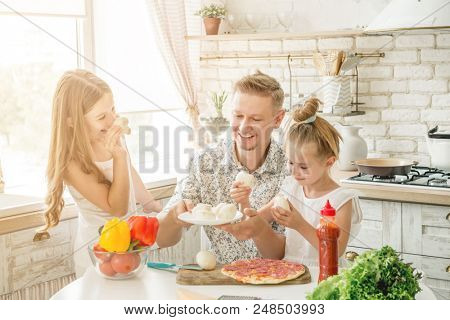 Dad with two small daughters preparing pizza with mushrooms in the kitchen