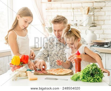dad with two little daughters preparing pizza in the kitchen