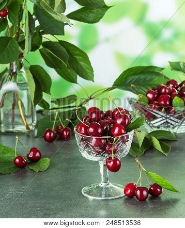 Crystal Vases With Ripe Cherries, Near On Gray Surface Three Berries