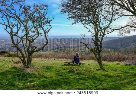 Rear View Of A Lady Sitting Contempating On A Bench In The South Downs National Park.  Admiring The 