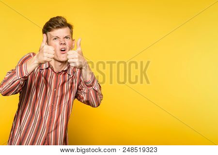 Approving Comic Funny Eccentric Man Showing Thumbs Up Gesture. Portrait Of A Young Guy On Yellow Bac