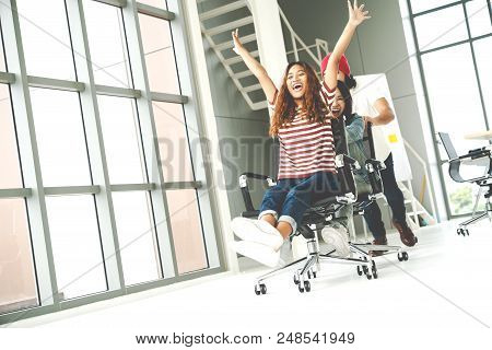 Group Of Multiethnic Young Creative Teamwork Having Fun Laughing And Smiling In Office Chairs Pushin