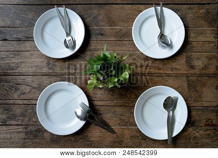 4 Empty Plates And Stanless Spoon And Fork On Dark Wooden Background. Top View With Copy Space