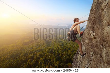 Joven sube en una pared rocosa en un valle con montañas al amanecer