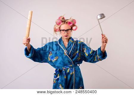 Serious Housewife In A Dressing Gown And Curlers With A Ladle And Battledore.