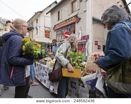 Briancon, France, 10 June 2018: People With Freshly Bought Plants And Flowers Buy Fruit On Open Air 