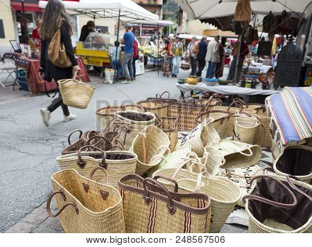 Briancon, France, 10 June 2018: Woman With Basket Passes A Lot Of Baskets For Sale On Open Air Marke
