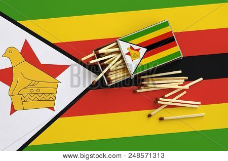 Zimbabwe Flag  Is Shown On An Open Matchbox, From Which Several Matches Fall And Lies On A Large Fla