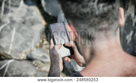 Over The Shoulder Shot Of A Young Man Using Cell Phone To Send Text Message, On A Beach