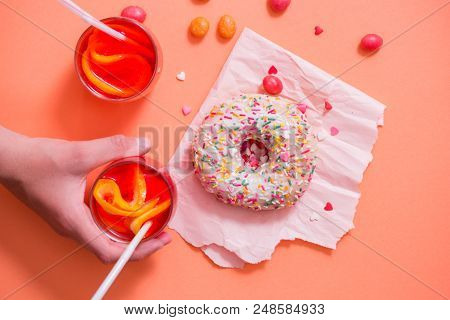 Child's Hand Takes Sweet Pastryfrosted Sprinkled Donut On Pink Background. Tubules For A Cocktail. S
