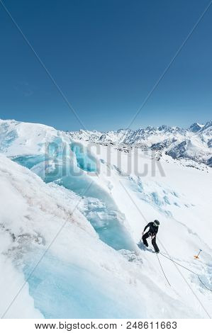 A Professional Mountaineer In A Helmet And Ski Mask On Insurance Makes A Nick-hole In The Glacier Ag