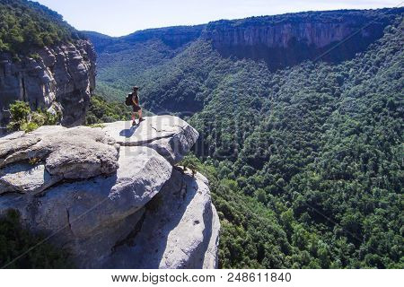 Risky Mountaineer On A Cliff Looking At The Horizon. Aerial View