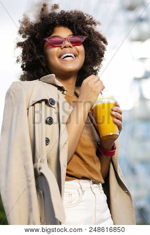 Happiest Smile. Beautiful Young Woman Smiling Belatedly And Drinking Orange Juice While Waiting For 