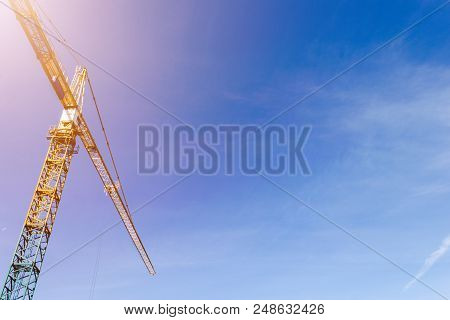 Construction Crane Tower On Blue Sky Background. Crane And Building Working Progress. Yellow Lifting