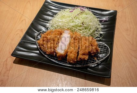 Fried Pork Tongkatsu With Vegetable In Black Ceramic Plate On Wood Table.