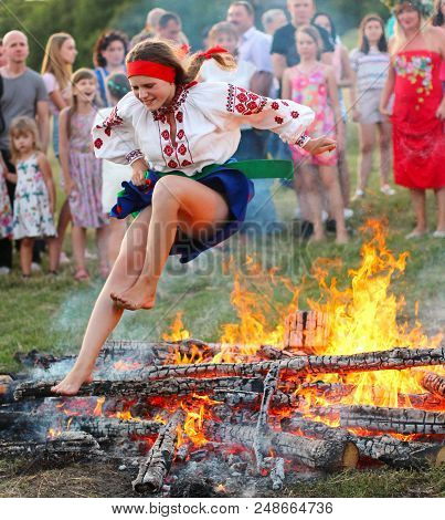 Kyiv, Ukraine - July 6, 2018: Young Girl In National Clothing Jumps Over The Flames Of Bonfire Durin