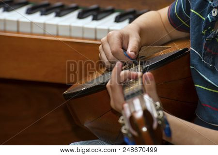 The Boy Plays The Guitar And Takes Chords, Dombra On The Background Of The Piano.