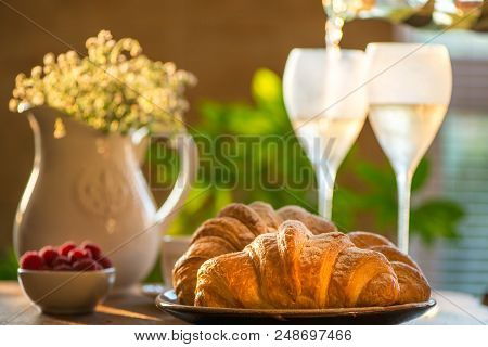 Fresh French Croissants With Rapberries And Pouring Sparkling Wine On Background. French Style Lunch