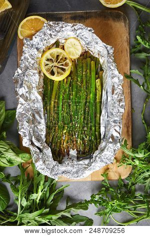 Cooking Food. Baked Asparagus With Lemon In Foil, Vintage Dish, Lemon, Basil And Ruccola On The Dark