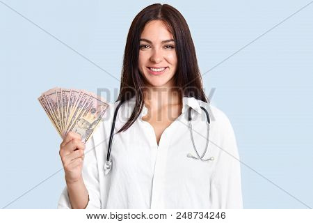 Cheerful Happy Brunette Female Doctor In White Robe, Holds Cash, Earns Salary By Curing Patients, St